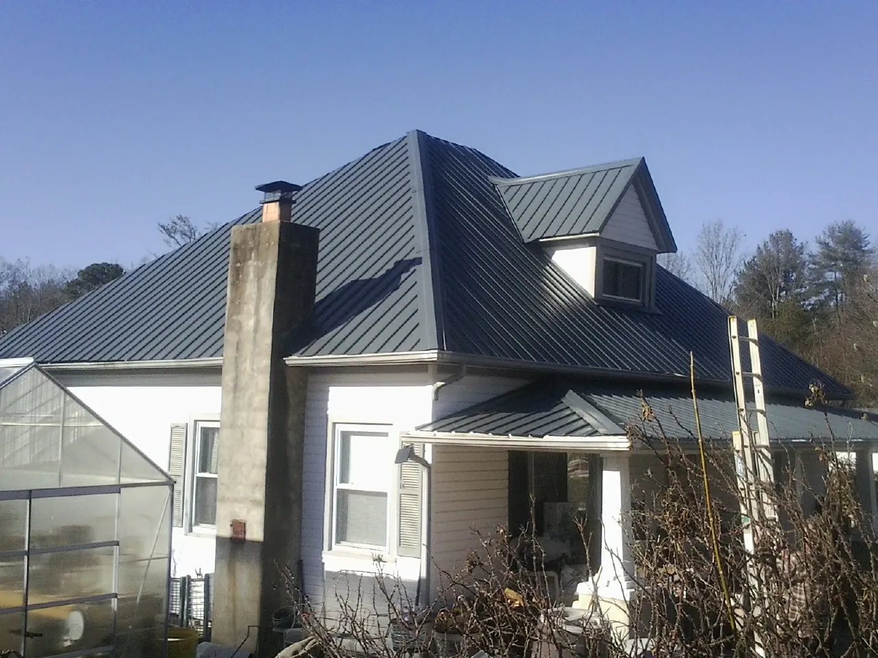 Dark blue standing seam metal roof on a white farmhouse with dormer — Slate & Tile Roof Repair by Roofing Brothers in West Townsend