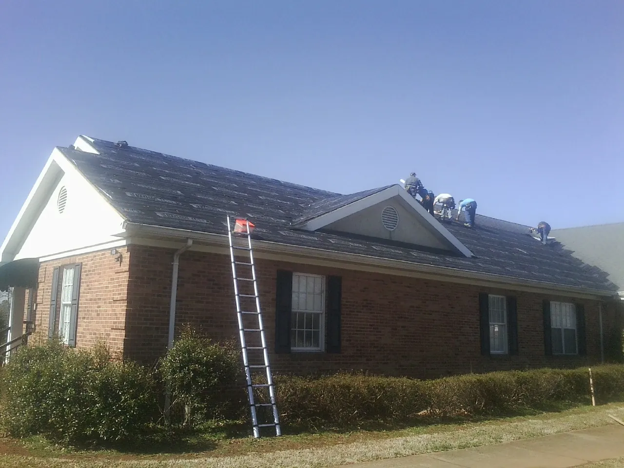 Crew tearing shingles off a brick ranch roof with a ladder set — Metal Roof Repair work by our crew in West Townsend