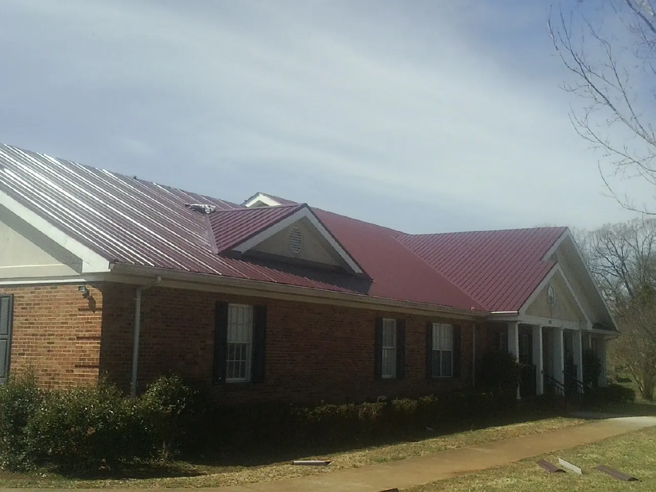 Red metal roof with gabled entries on a long brick building, from a Hail Damage Roof Repair job in West Townsend