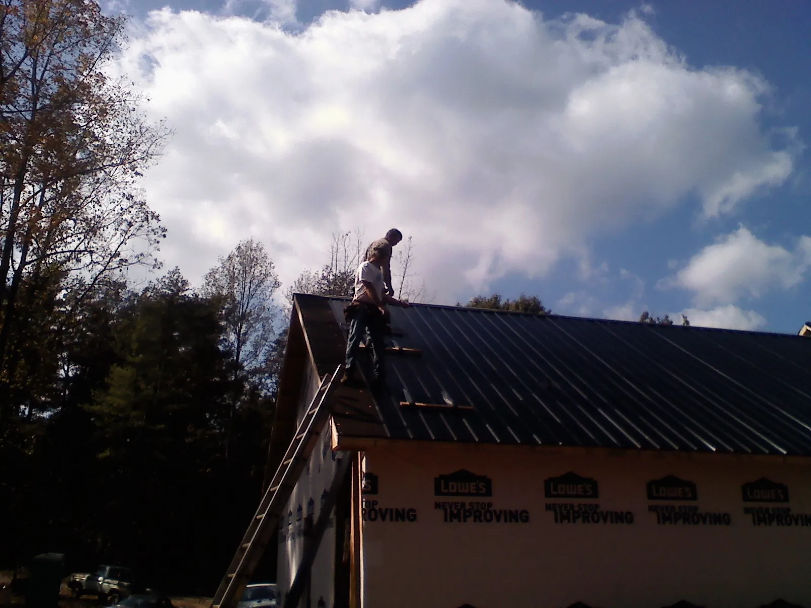 Roofer fastening dark metal panels high against a cloudy sky, from a Roof Inspection job in West Townsend