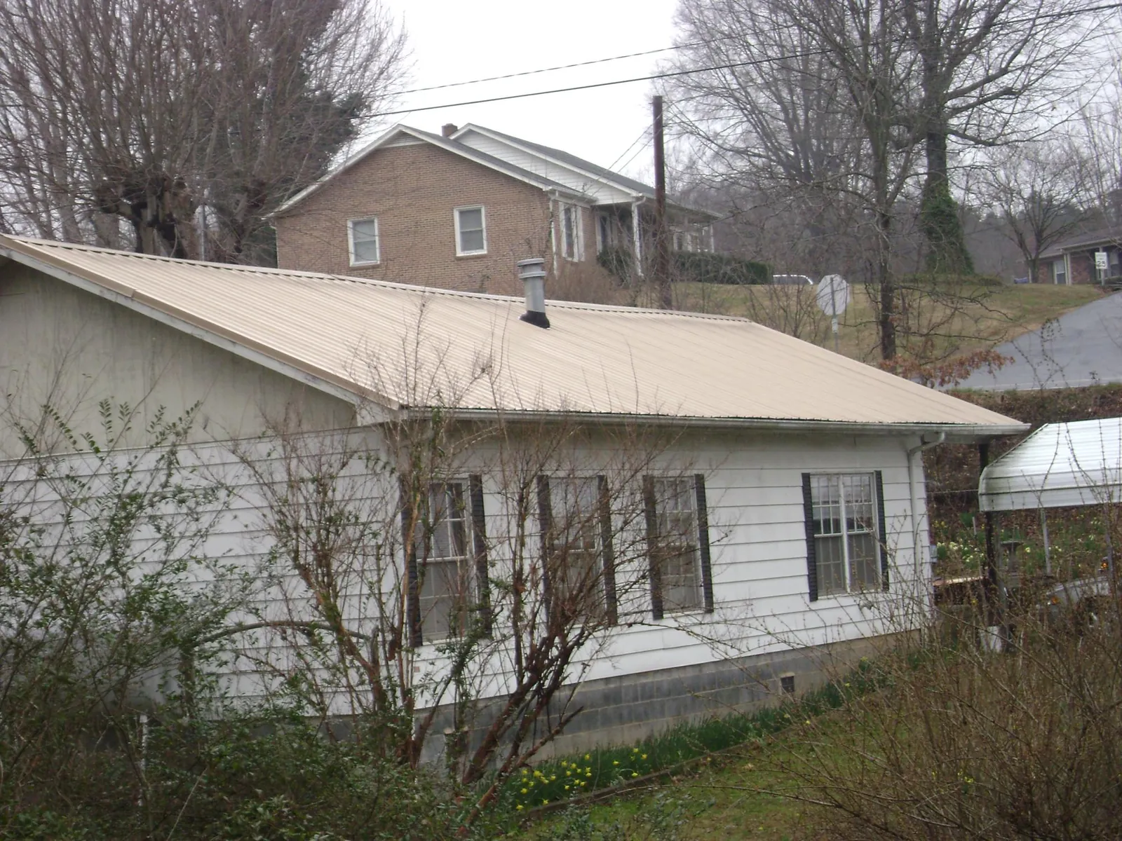 Tan metal roof on a white sided house set into a hillside — Commercial Roofing by Roofing Brothers in West Townsend